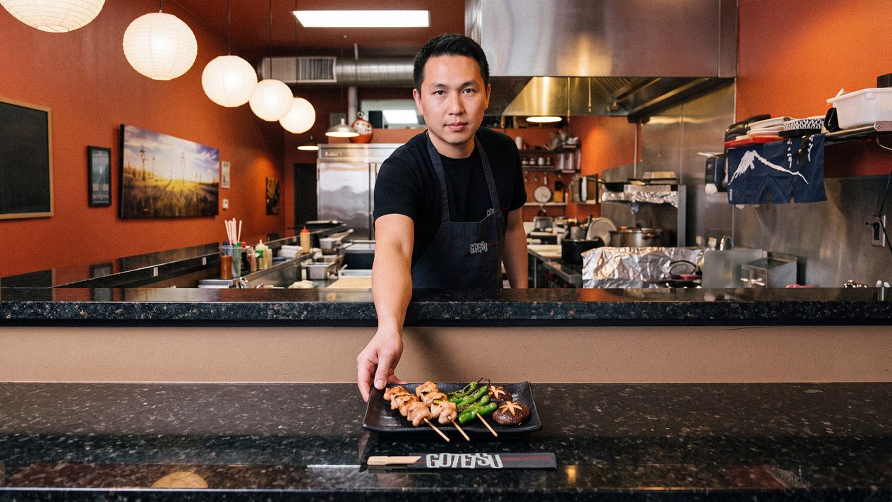 A Gotetsu cook setting a plate of kushiyaki skewers down on the counter, a branded chopstick rest in front of him.
