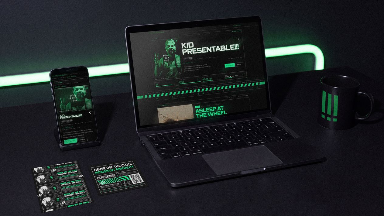 The Kid Presentable!!! website on a laptop and phone on a black desk under a green neon strip, with a branded mug and stacked show cards.