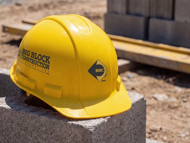 A yellow Big Block Construction hard hat resting on a concrete block on site.