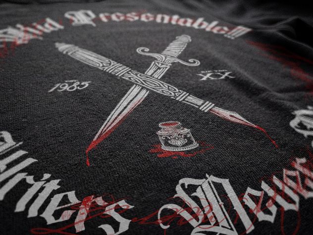 Macro of the Kid Presentable!!! shirt print: a crossed dagger and dip pen over a spilled inkwell, in white and red blackletter on black fabric.