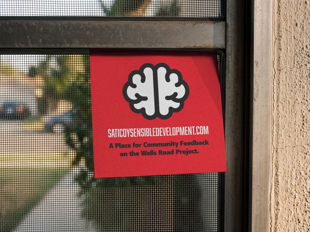 A red Saticoy Sensible Development card taped inside a window: a white brain mark, the web address, and the line A place for community feedback on the Wells Road project.