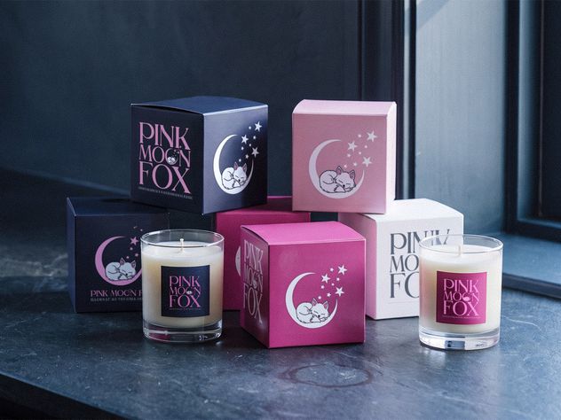 Six Pink Moon Fox boxes stacked with two candles, in navy, pink, magenta and white, each carrying the sleeping fox and crescent moon mark.